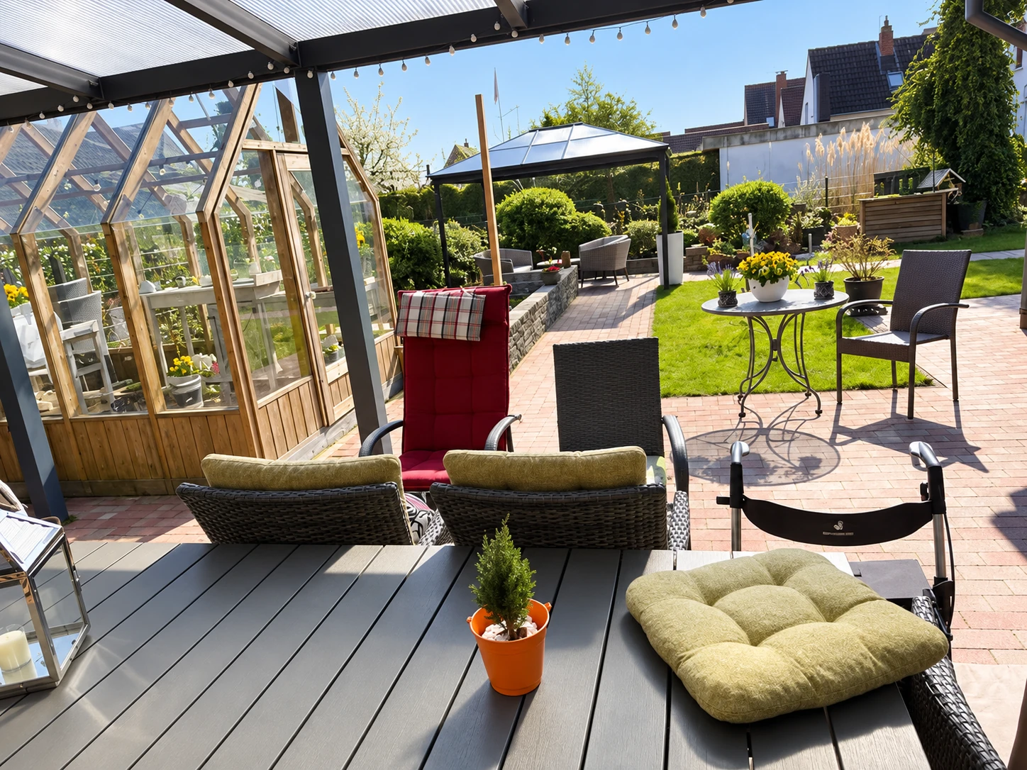 Garten und Sonnenterrasse mit Sitzgelegenheiten und Gewächshaus; abgebildete Personen mittels KI entfernt.